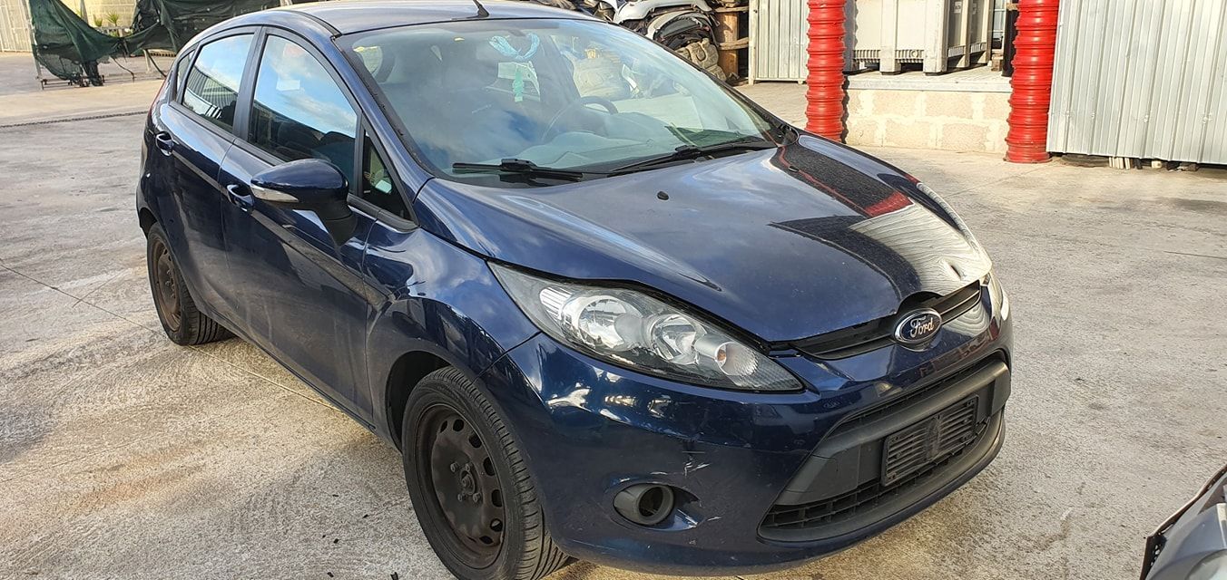 Una Ford Fiesta hatchback blu scuro parcheggiata su un piazzale ghiaioso.