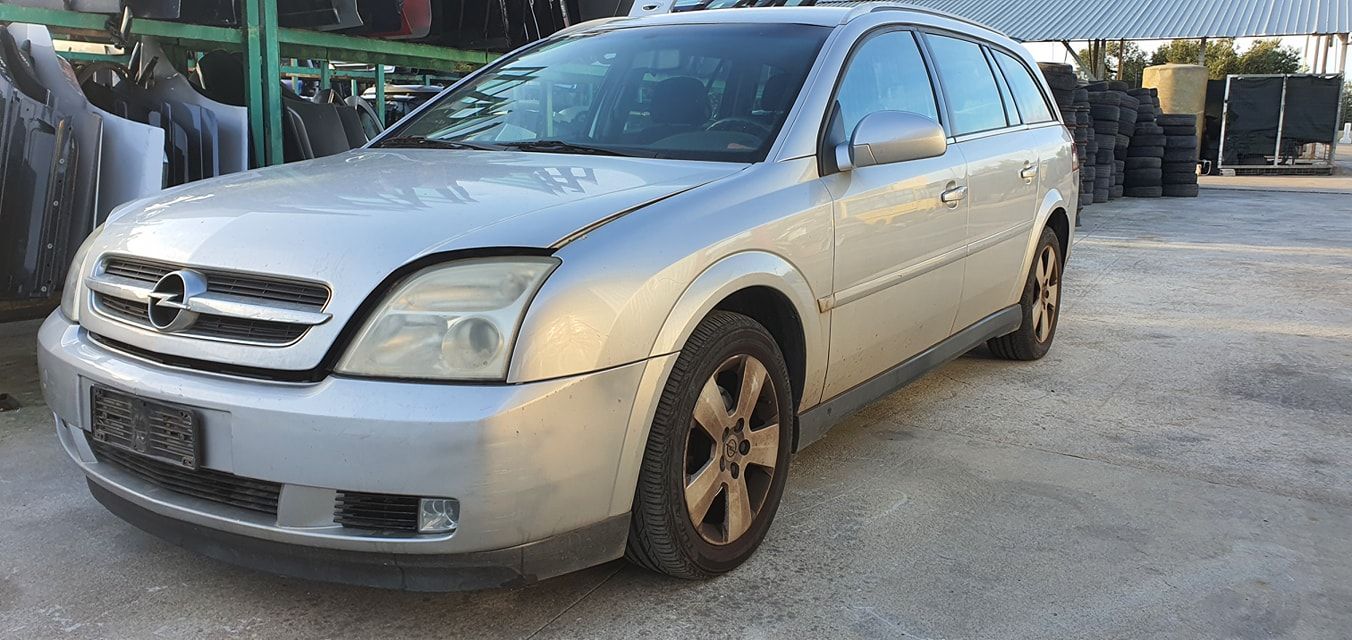 Una station wagon argentata parcheggiata in un deposito di rottami all'aperto, vista dal lato anteriore del passeggero.