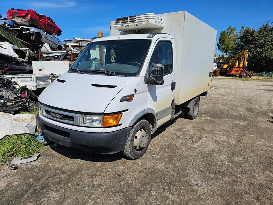 Un furgone Iveco bianco con unità di refrigerazione montata sul tetto, parcheggiato in un deposito di rottami industriali.