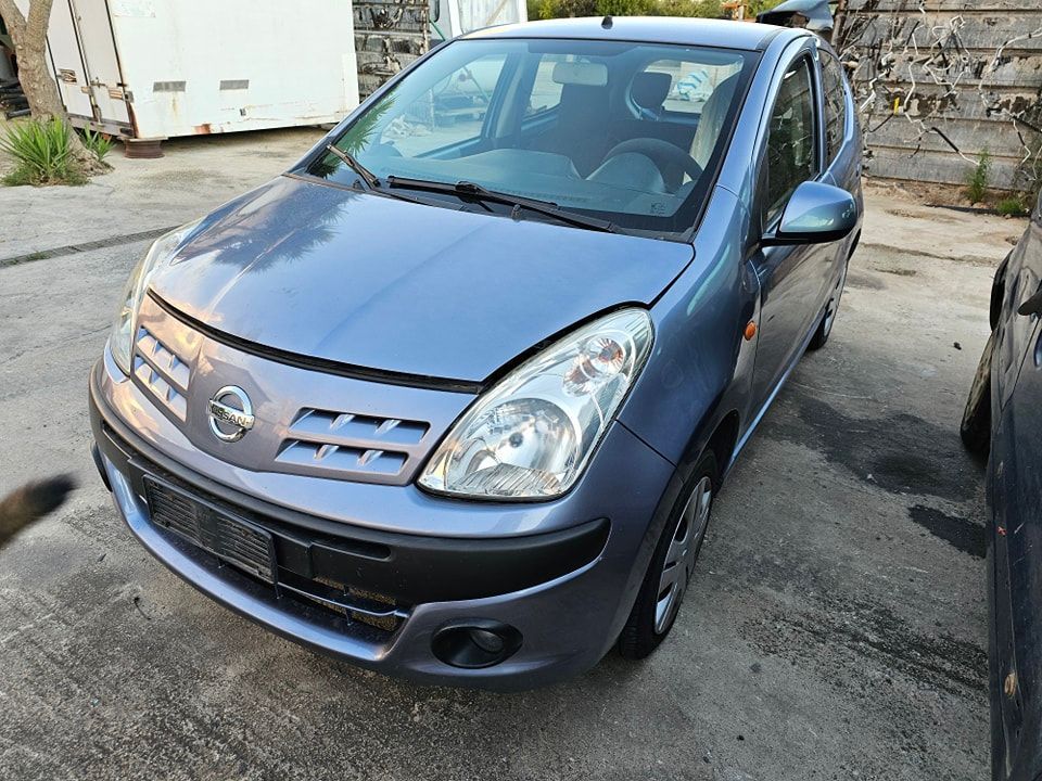 Una Nissan Note azzurra parcheggiata all'aperto su una superficie di cemento, vista di tre quarti anteriore.