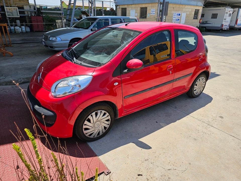 Un'auto hatchback rossa parcheggiata su un piazzale di cemento in una giornata di sole.