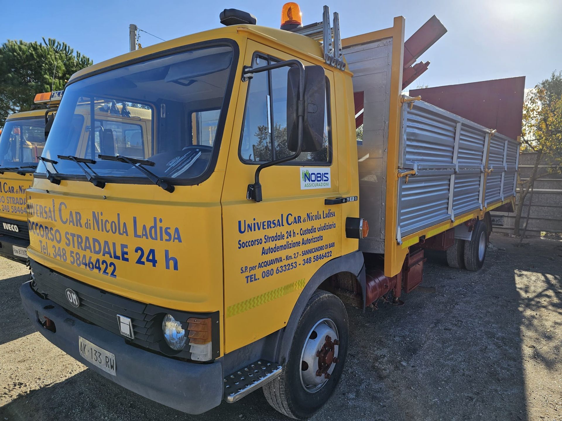 Camion Universal Car giallo con pianale, parcheggiato in un parcheggio all'aperto in una giornata di sole.