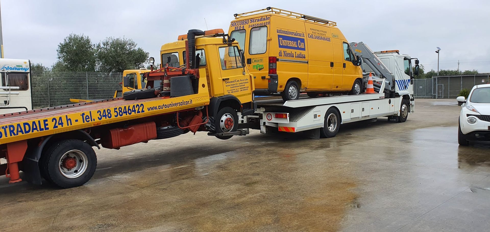 In una giornata nuvolosa, un carro attrezzi giallo trasporta un furgone di servizio giallo sul suo pianale in un parcheggio all'aperto.