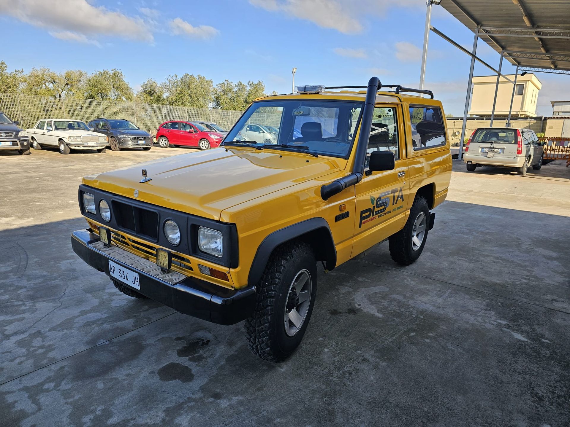 Un SUV giallo brillante a due porte con snorkel, parcheggiato in un parcheggio all'aperto in una giornata di sole.