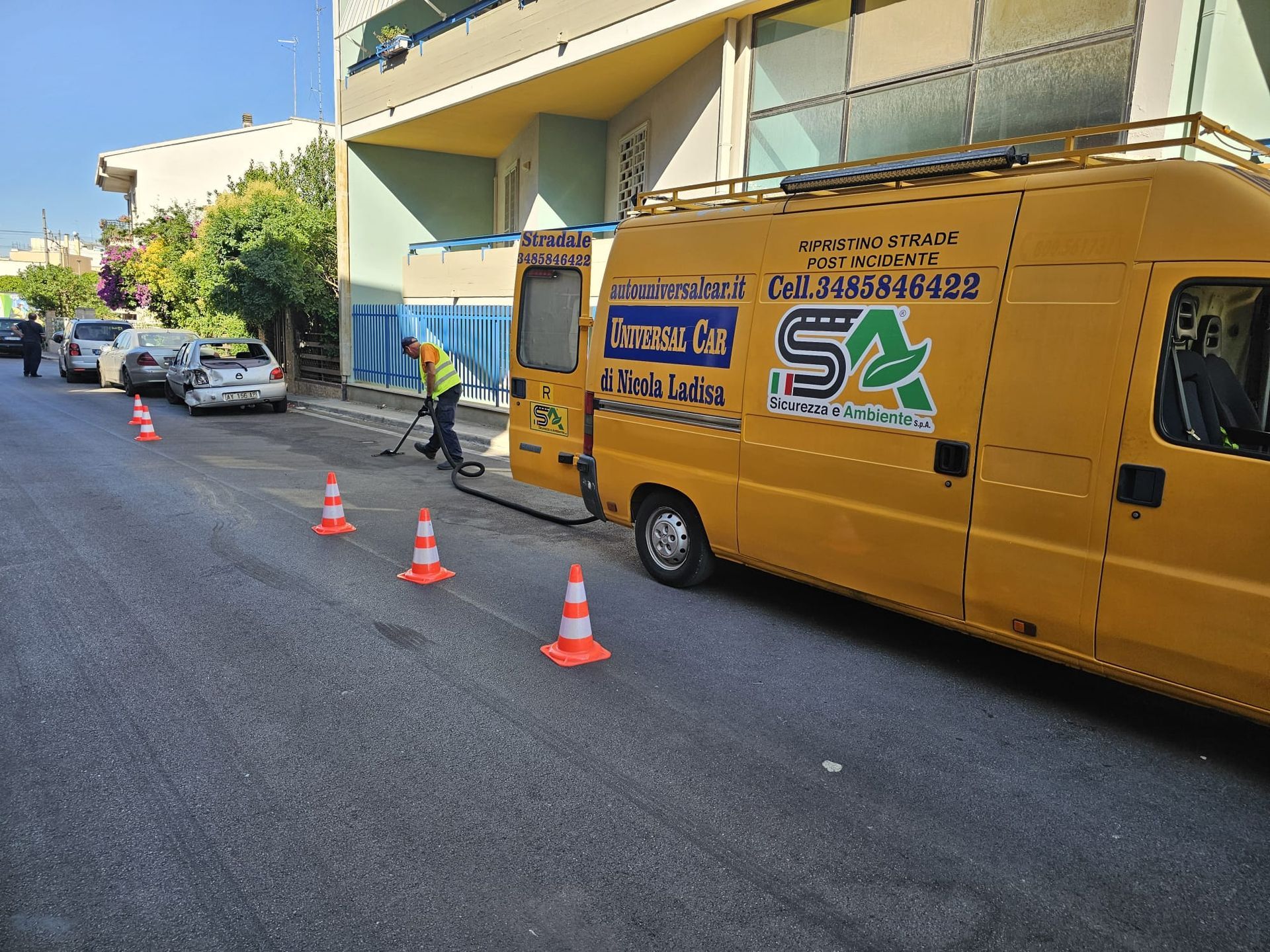 Un operaio con un giubbotto ad alta visibilità esegue lavori stradali vicino a un furgone giallo di servizio contrassegnato dal logo