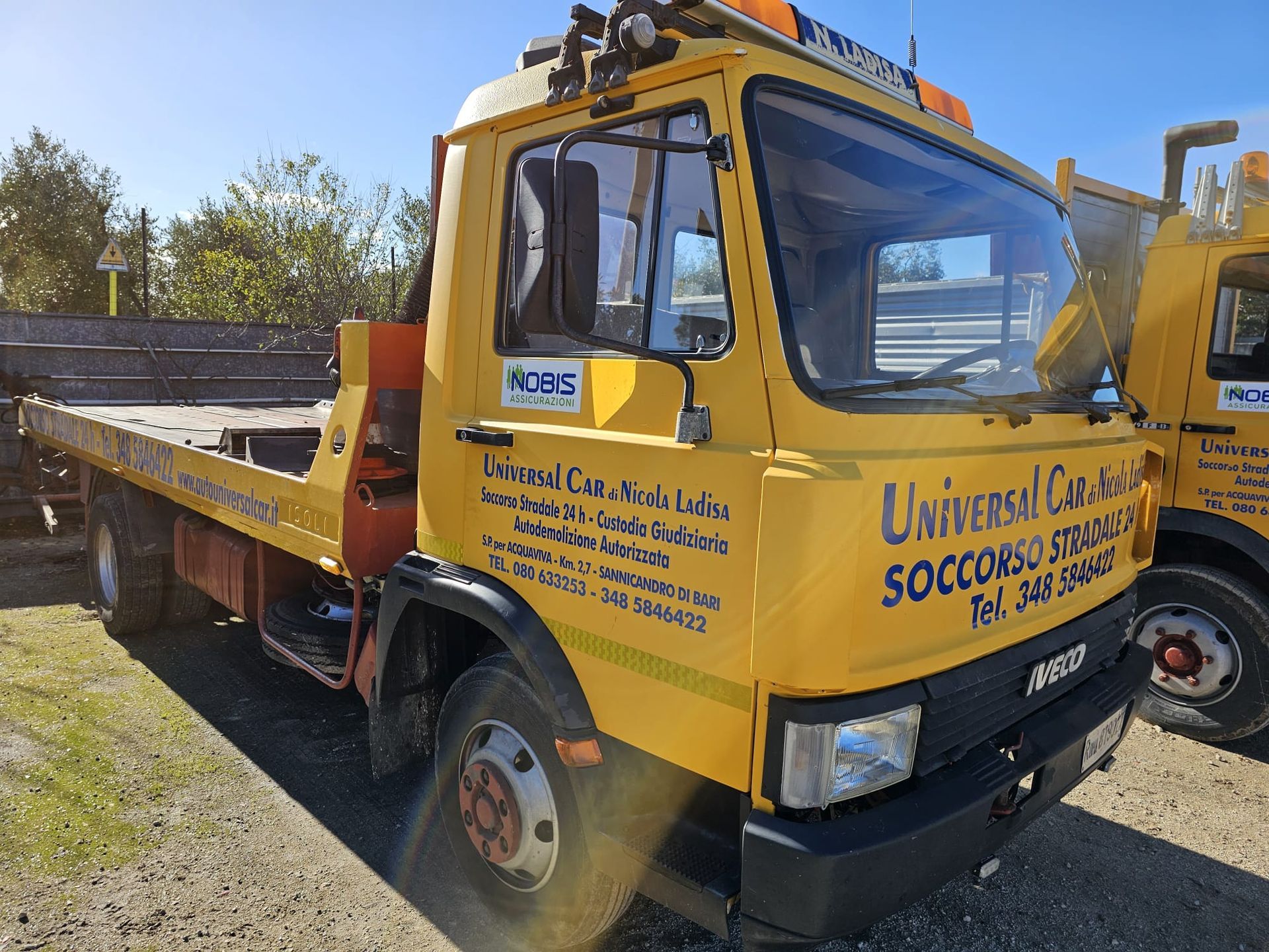 Un carro attrezzi Iveco giallo parcheggiato all'aperto su un piazzale ghiaioso, visto dall'alto.