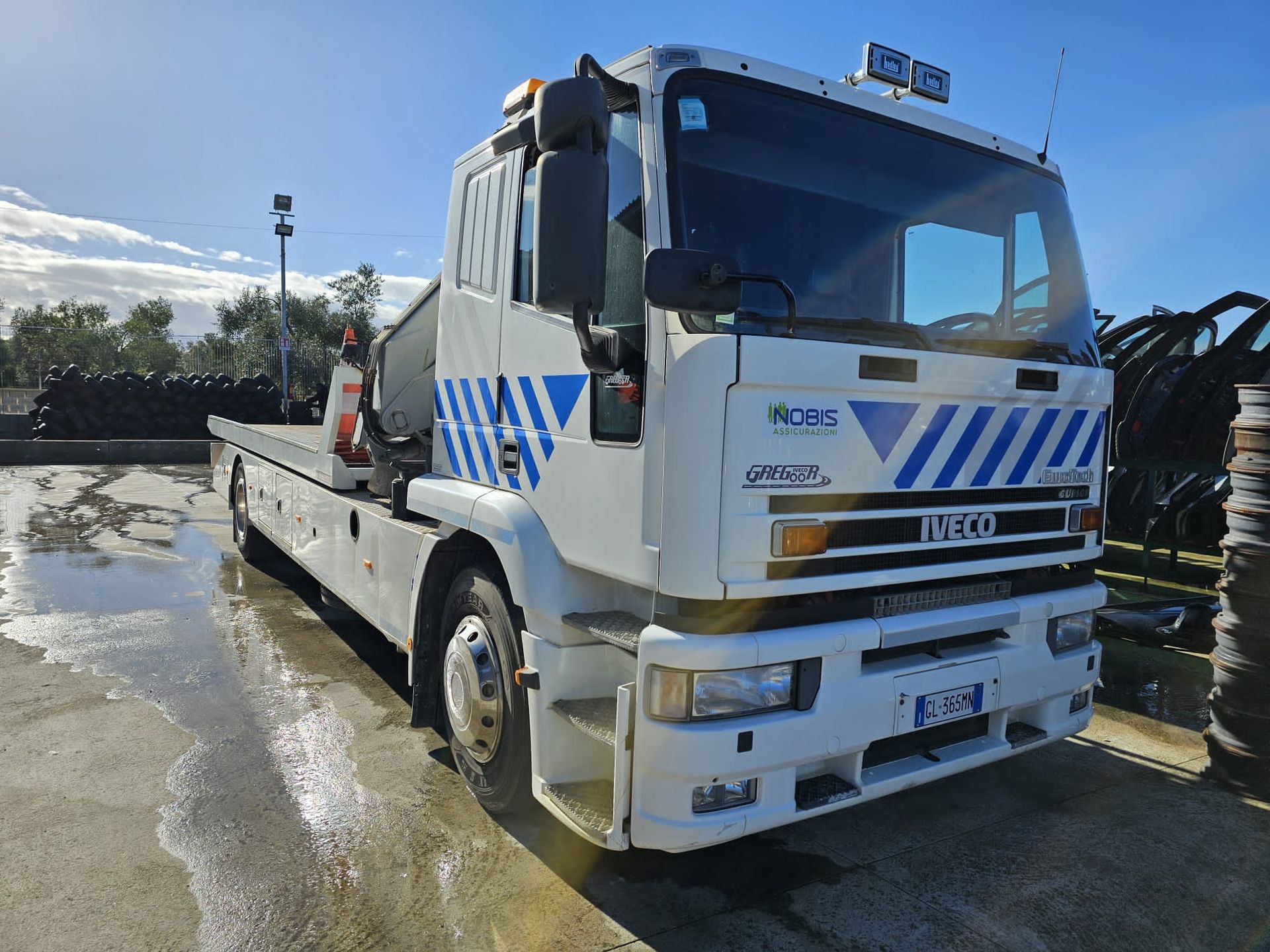 Carro attrezzi Iveco bianco parcheggiato all'aperto, sotto un cielo soleggiato, su una superficie asfaltata.