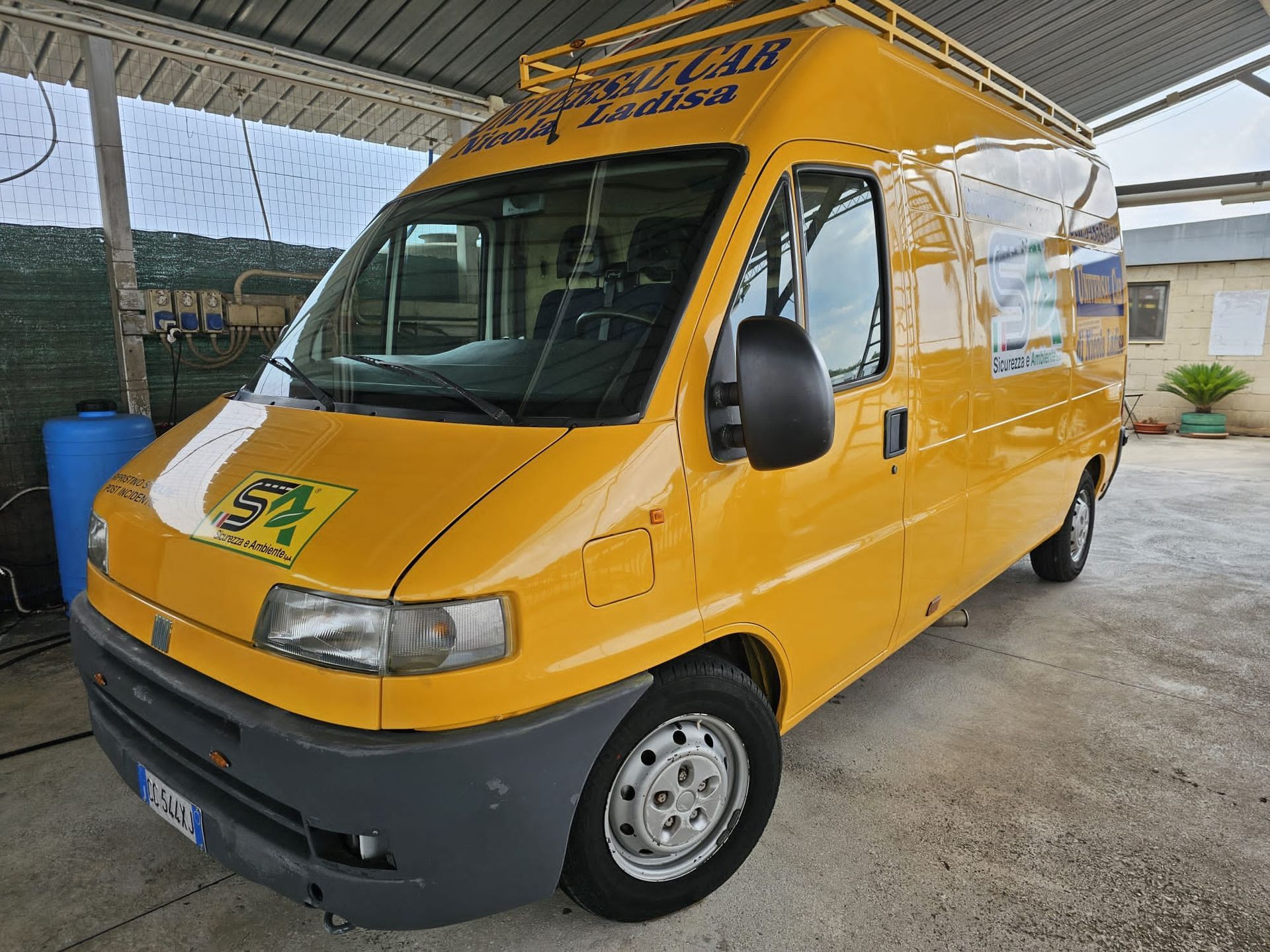 Un furgone Fiat Ducato giallo per le consegne, parcheggiato all'aperto, con portapacchi sul tetto e loghi aziendali sui lati e sul cofano.