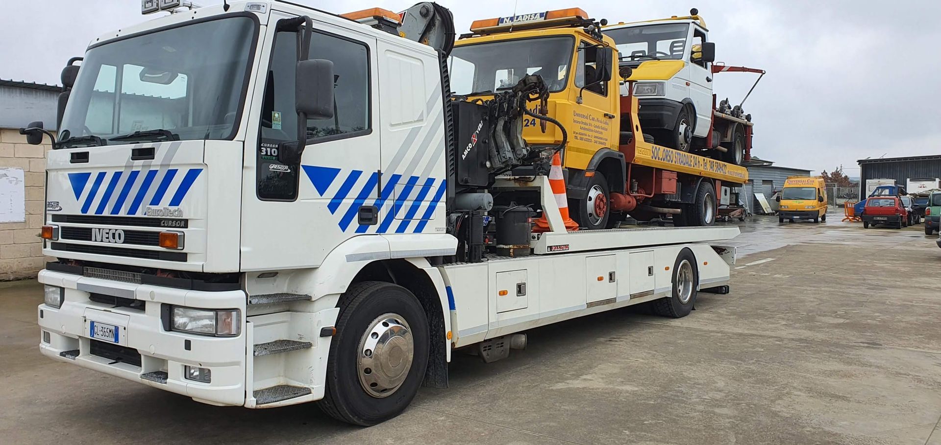 Un carro attrezzi bianco parcheggiato all'aperto, con un camion giallo sul pianale.