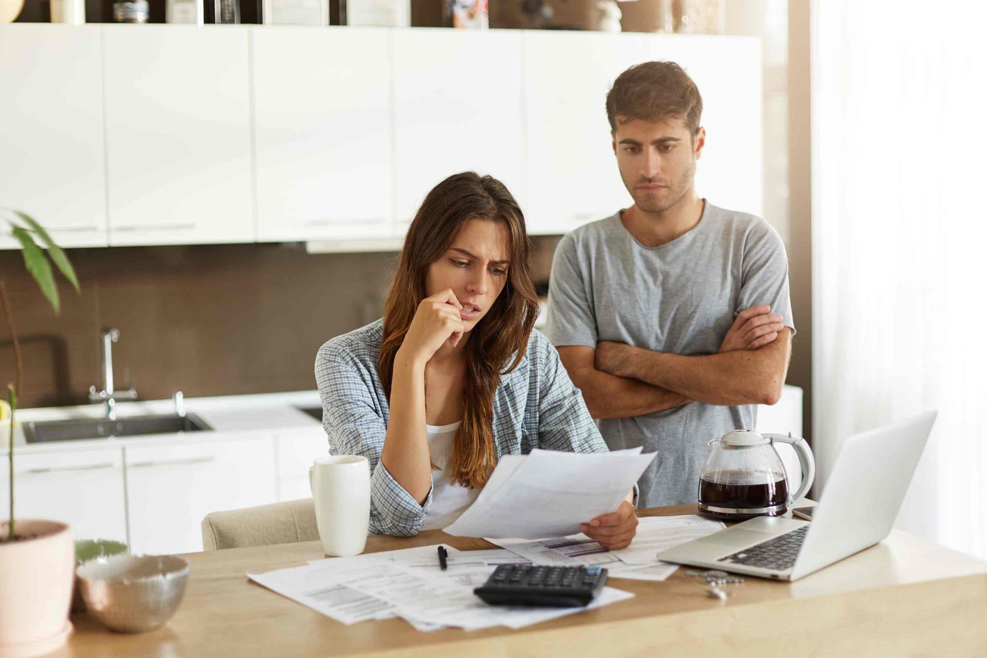 A man and a woman are sitting at a table with papers and a laptop.