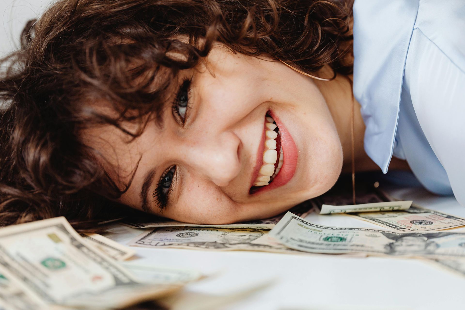 Woman smiling, lying on a white surface covered in US currency.
