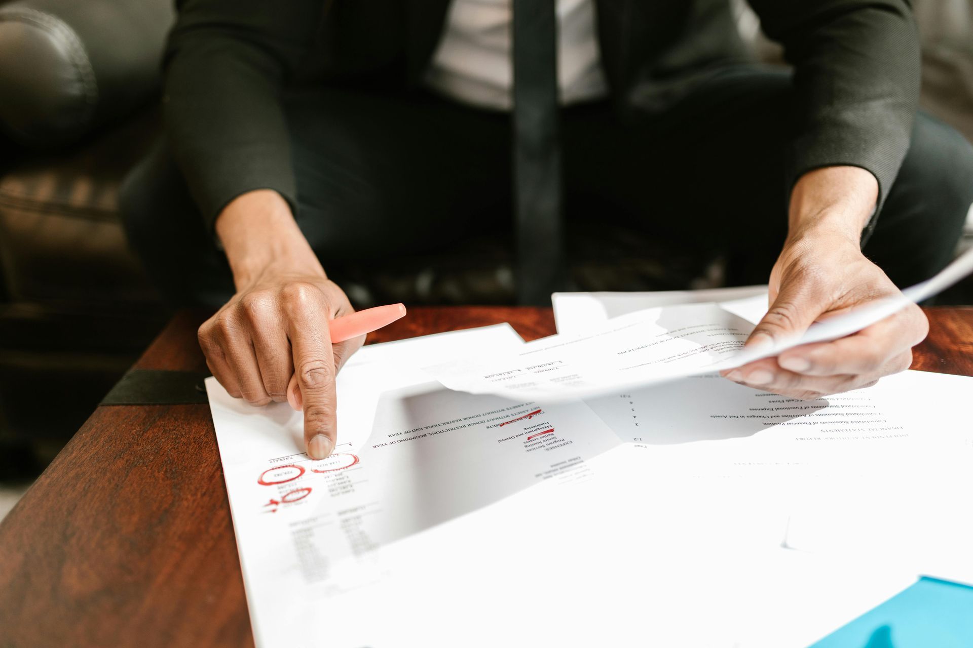 Person in suit pointing at documents on a table, holding a pen.