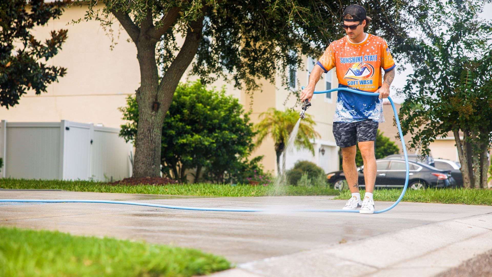 A man is using a hose to clean a driveway.
