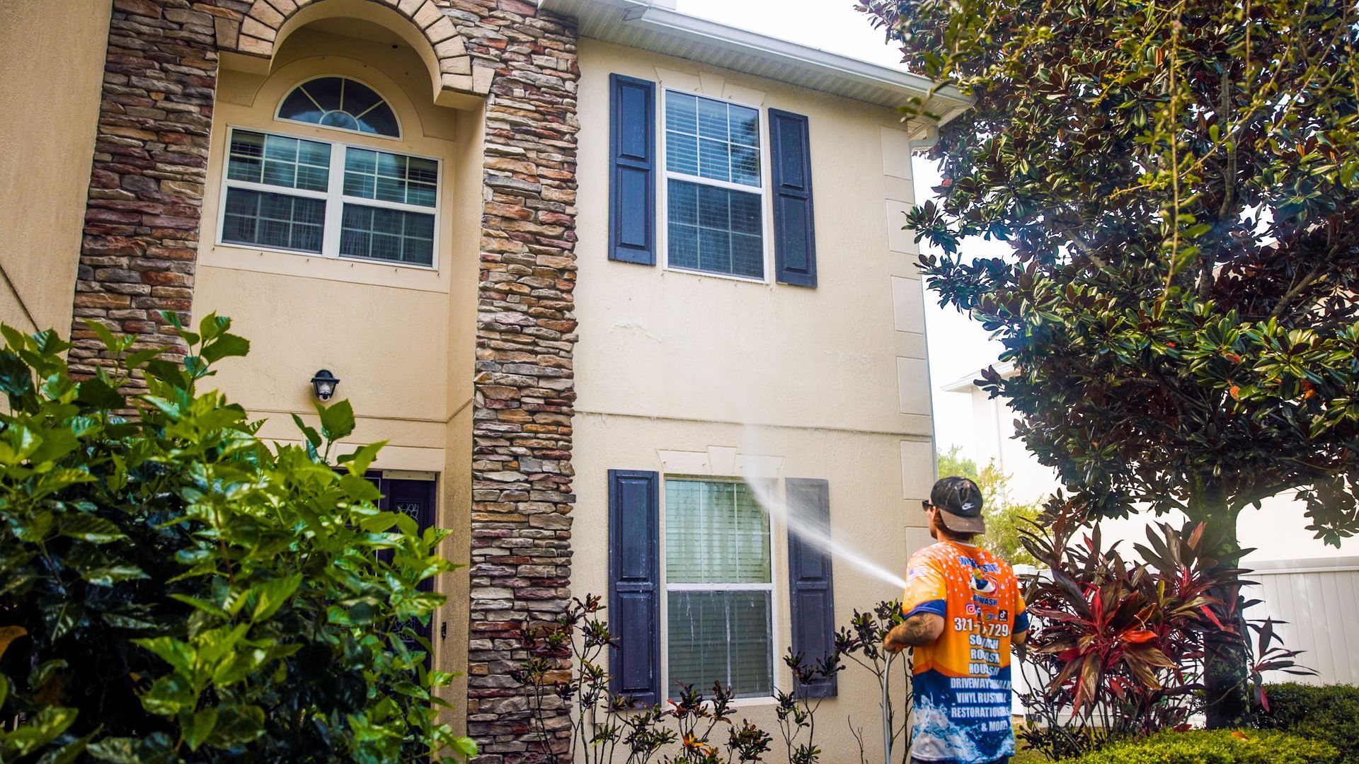 A man is spraying water on the side of a house.