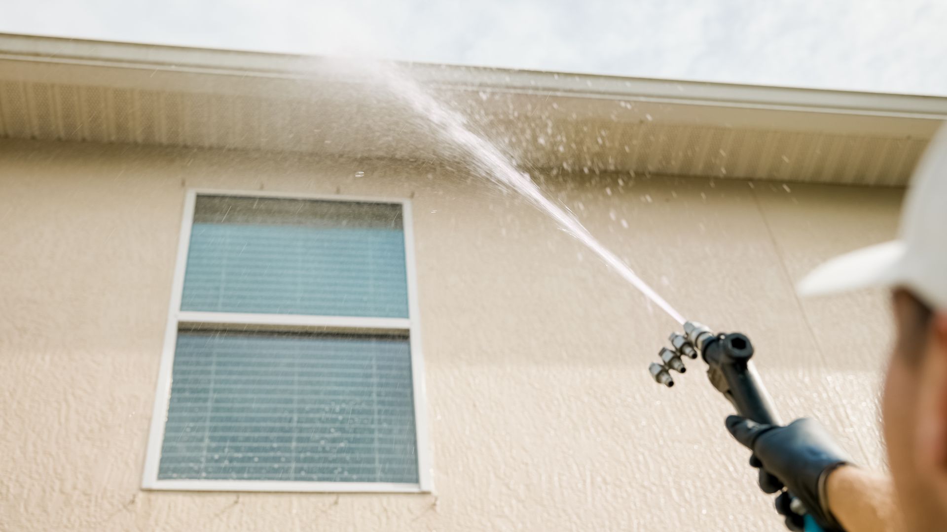 Person using a pressure washer on the side of a house, cleaning the siding.