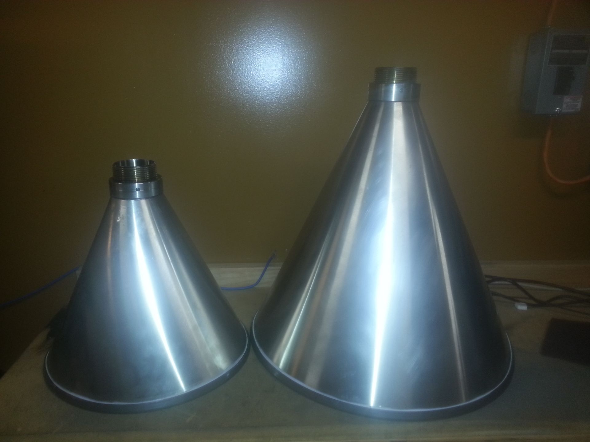 Two silver metal cone-shaped objects on a wooden surface, with a light-colored wall in the background.