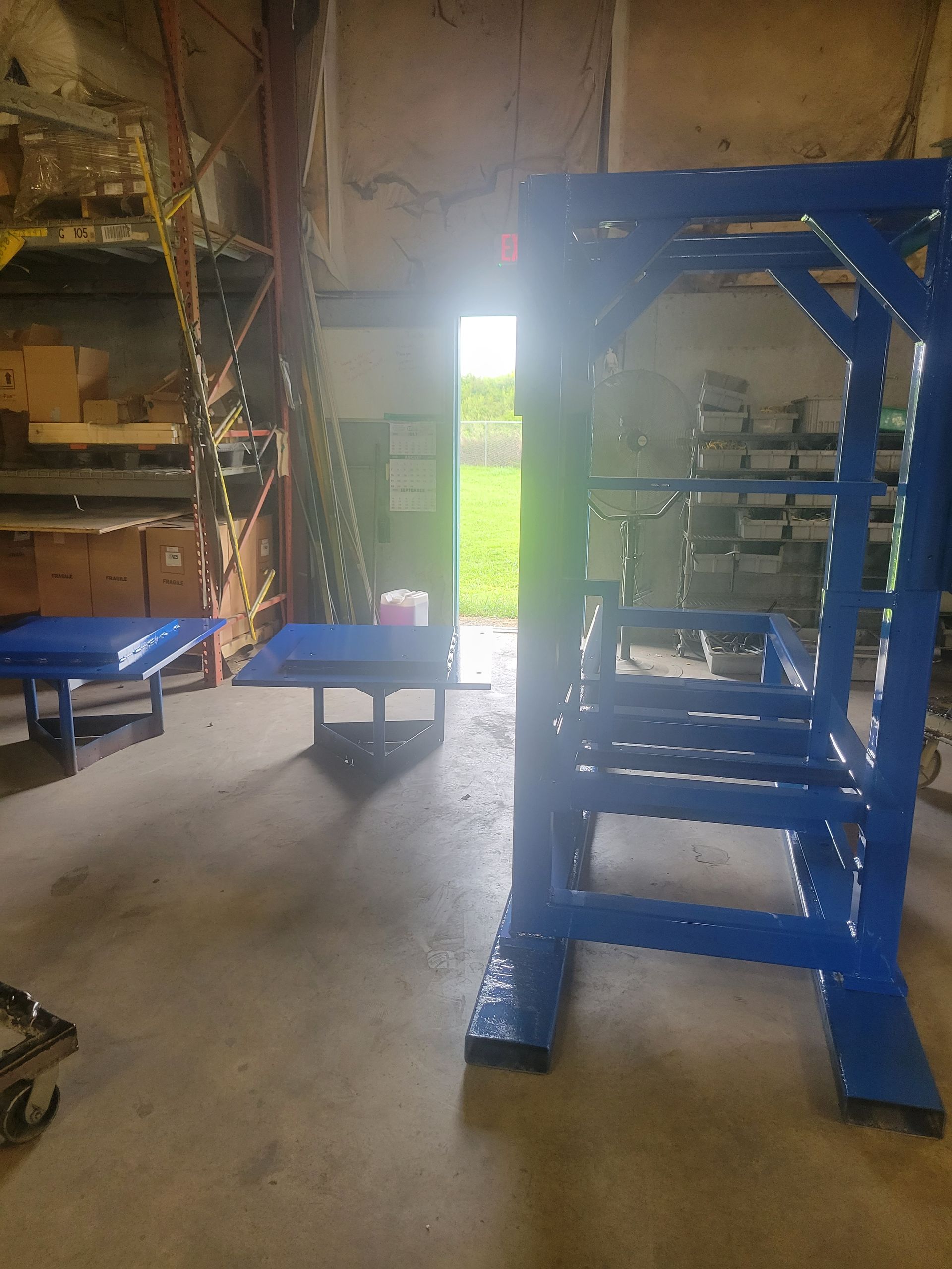Blue weightlifting rack and bench in a garage. Bright sunlight shines through an open doorway.