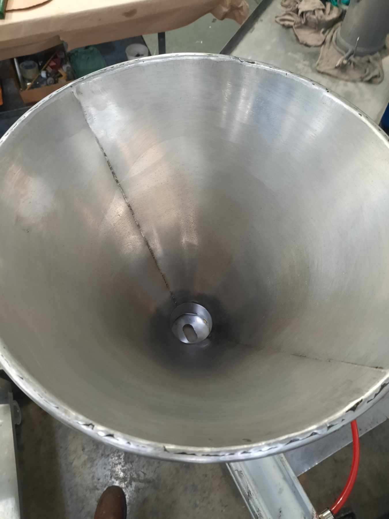 Inside of a metallic conical funnel with a central fitting and visible welding lines.