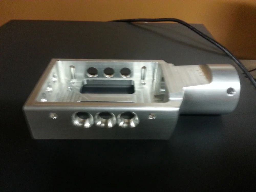 Silver metal machined component with multiple holes and a cylindrical extension, on a dark surface.