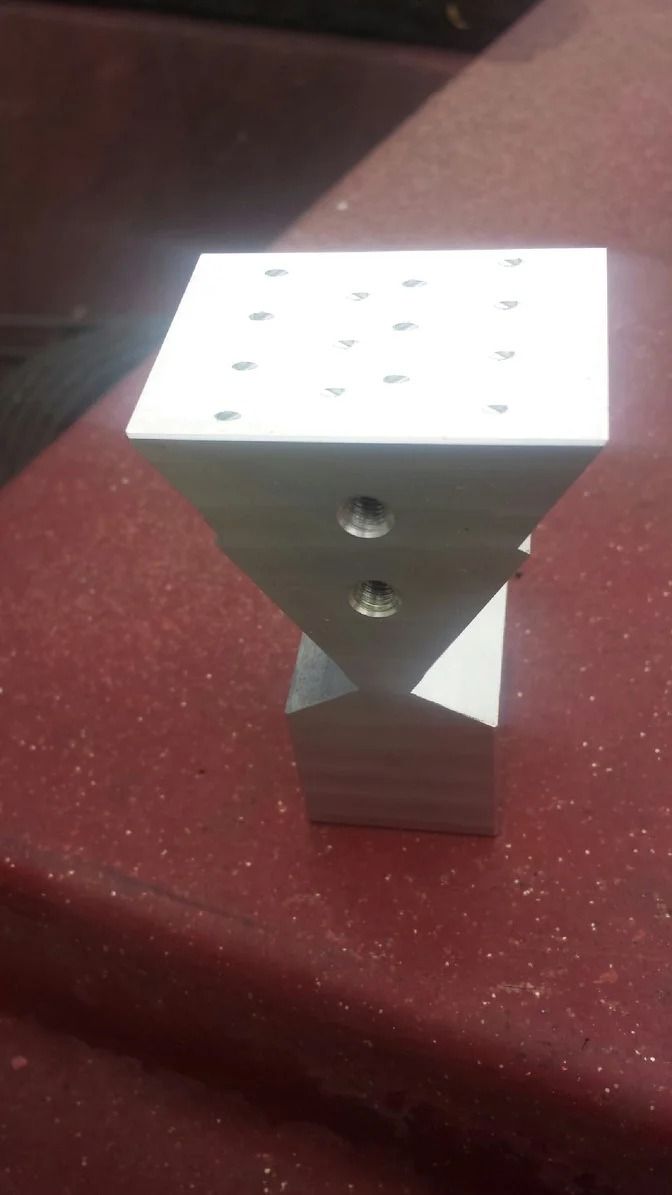 Silver metal object with a square top, twisted middle section, and square base, with drilled holes.