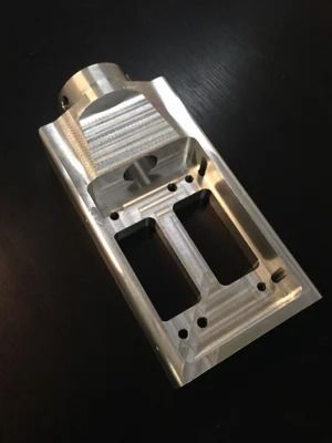 Machined aluminum part with two rectangular openings, cylindrical attachment, and drilled holes.