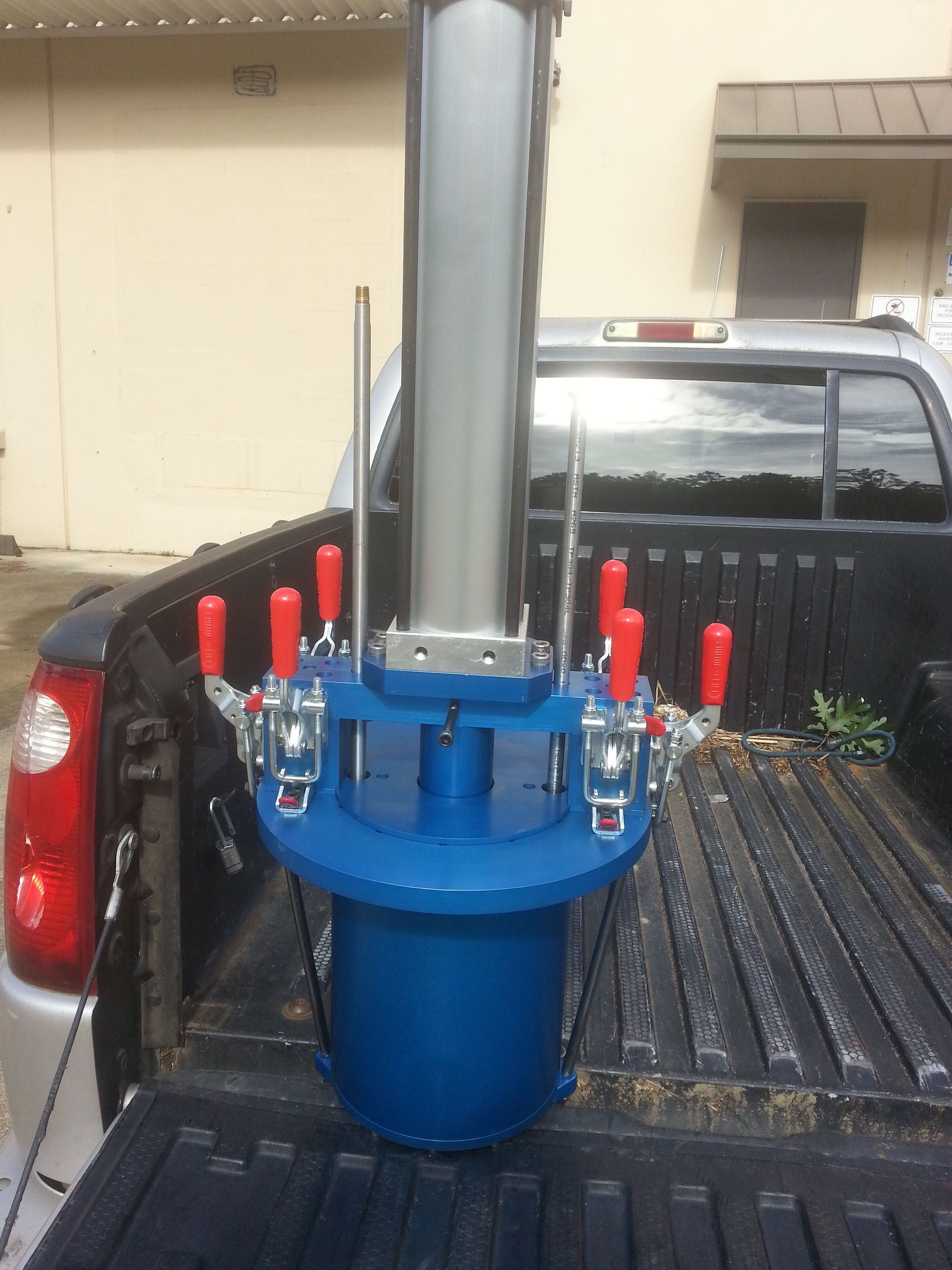 Blue and silver industrial equipment in the bed of a pickup truck. Red handles. Outdoors.