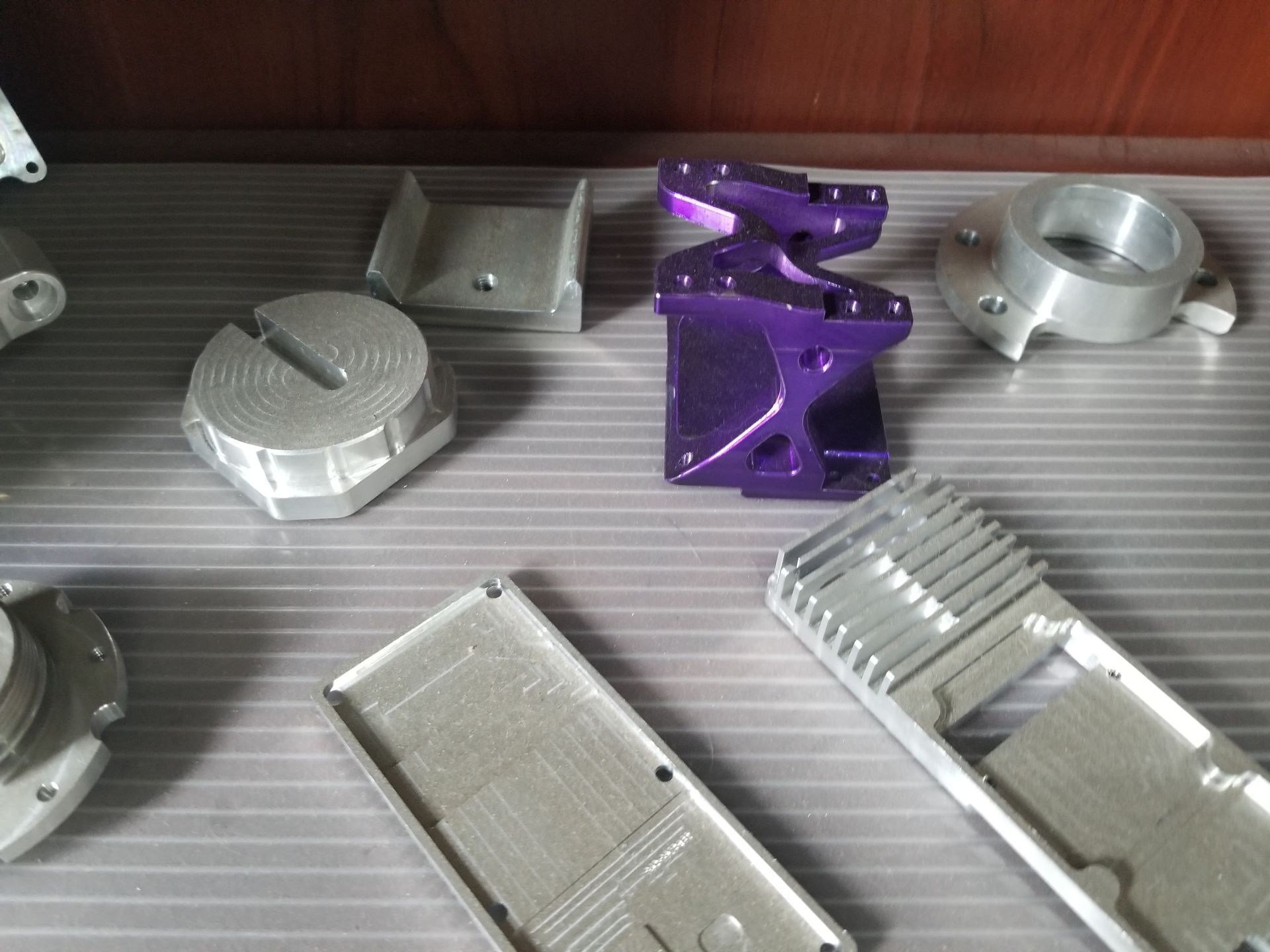 Various machined metal parts, some silver, one purple, on a shelf.