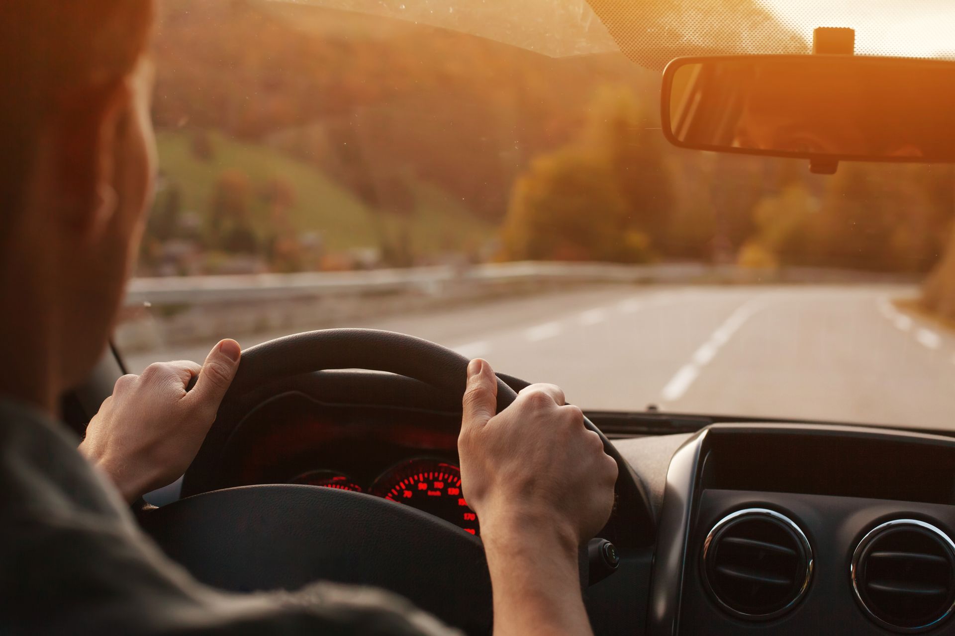 Driver gripping the wheel on a sunlit road at sunset, viewed from inside the car | Ron's Auto & RV