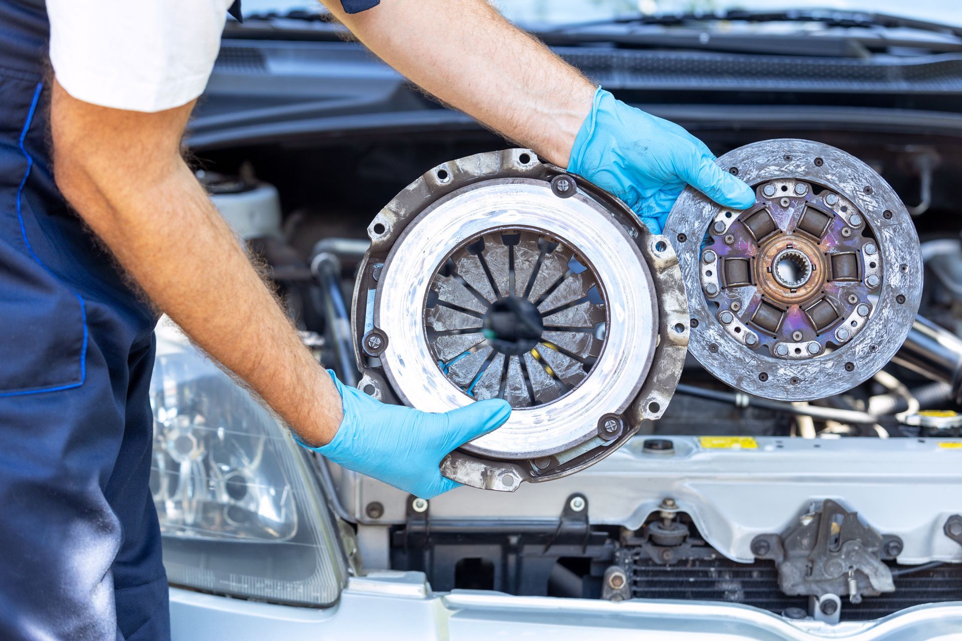 Mechanic in blue gloves holding a clutch kit in front of an open car engine bay | Ron's Auto & RV