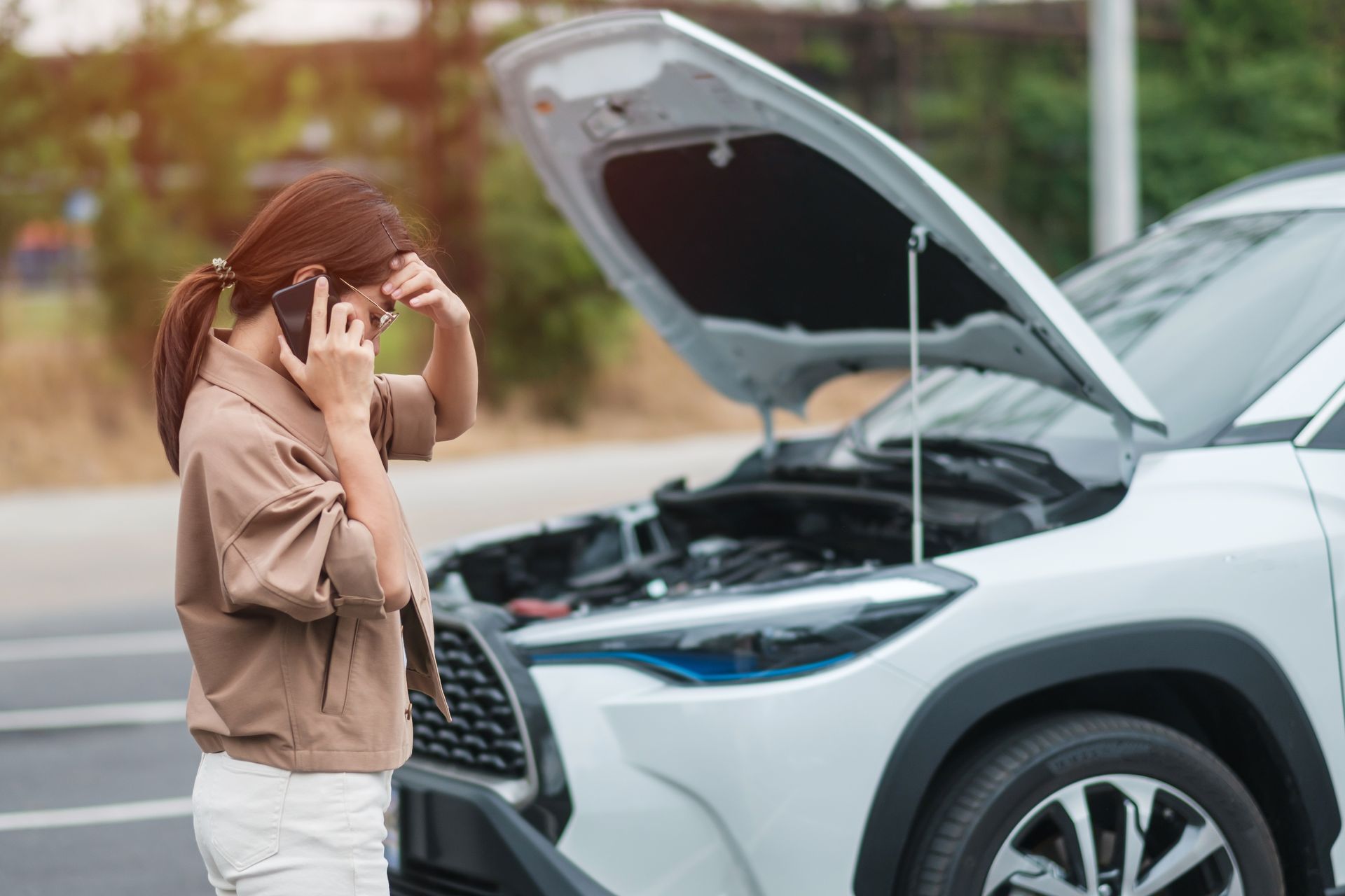 Woman standing by a silver car with its hood open, holding her head in concern. | Ron's Auto & RV