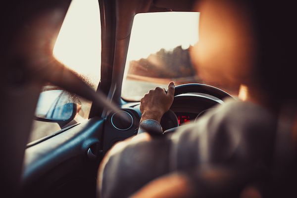 Driver's hand on the steering wheel inside a car at sunset, seen from the back seat. | Ron's Auto & RV