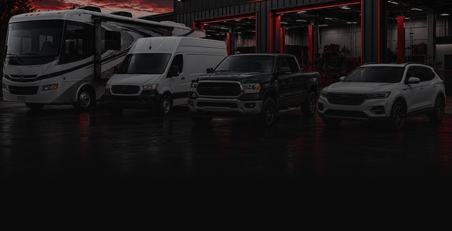 Several vehicles, including a bus, vans, and SUVs, parked in front of a modern building at dusk | Ron's Auto & RV