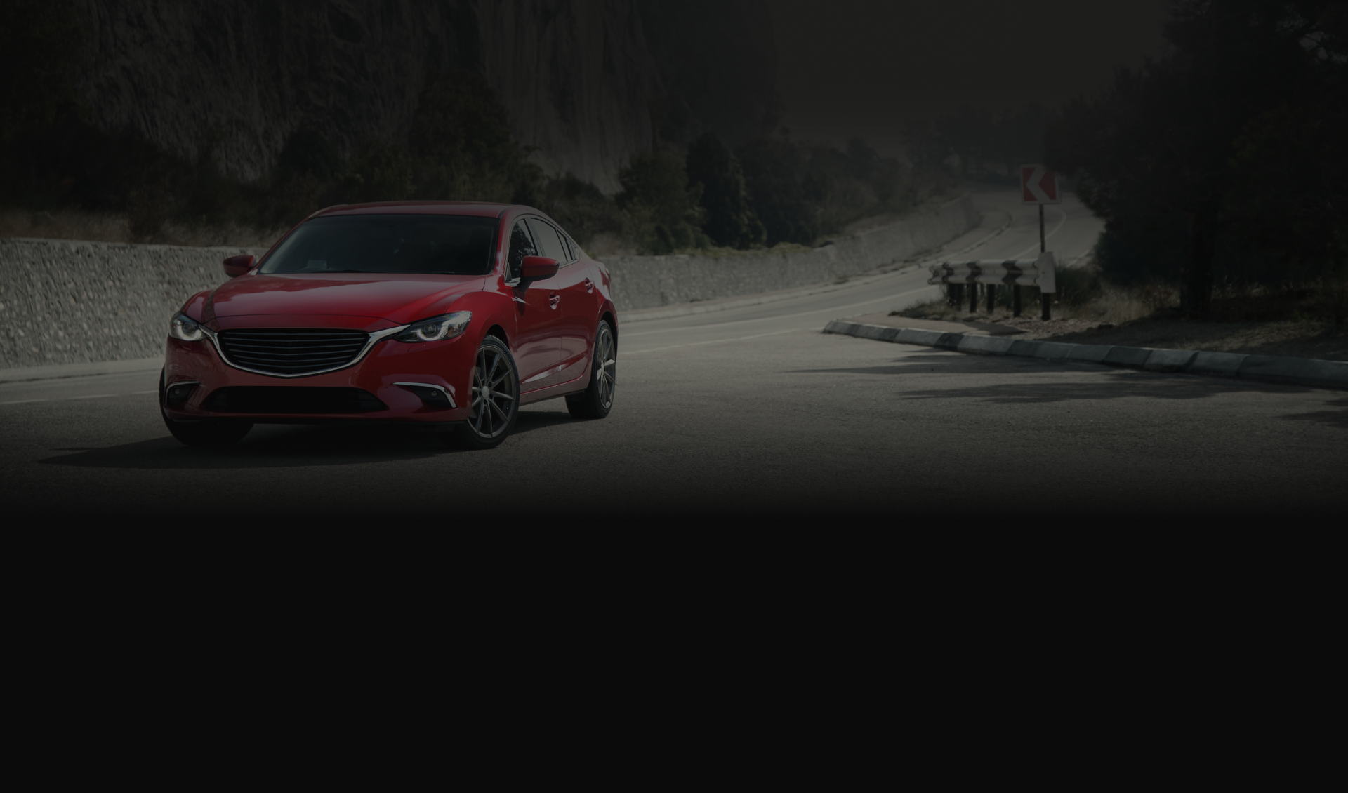 Red sedan driving on a wet road through a dark, foggy forest bend | Ron's Auto & RV