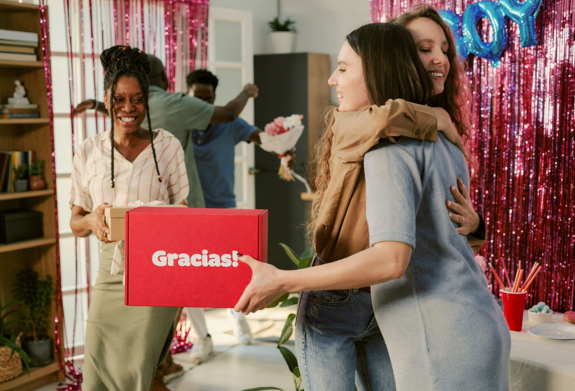 Em uma festa, pessoas comemoram: uma mulher segura uma caixa de presente rosa escrito 