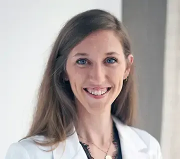 A woman in a white lab coat is smiling for the camera.