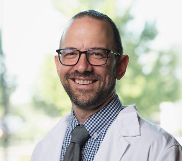 A man in a lab coat and tie is smiling for the camera.