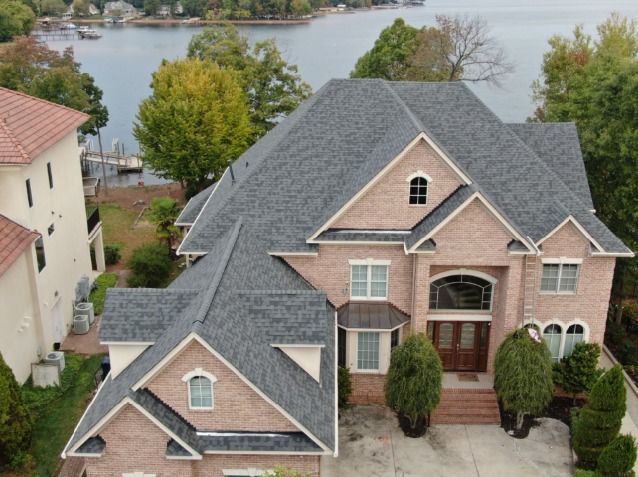 An aerial view of a large brick house with a lake in the background