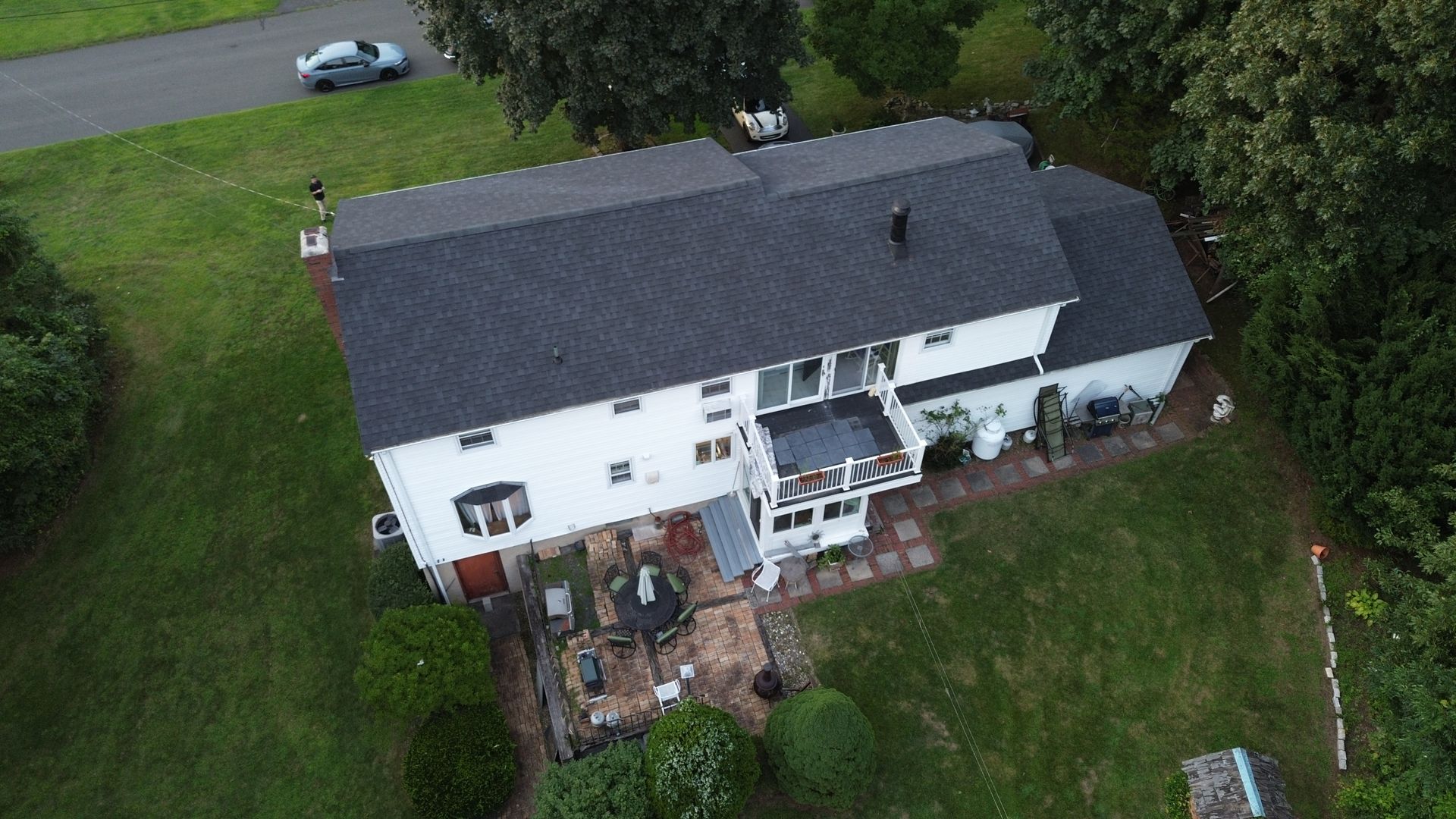 An aerial view of a large white house with a black roof surrounded by trees and grass.