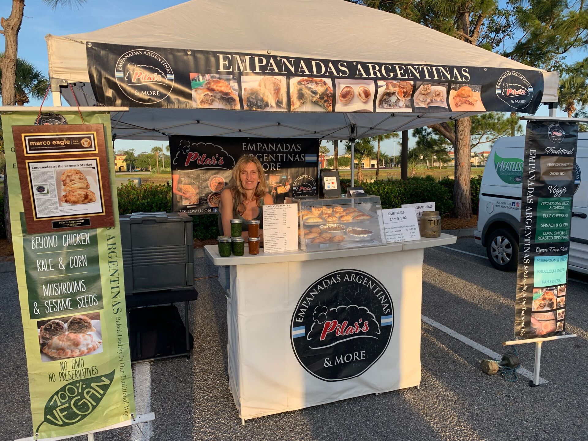 Empanadas Argentinas food stall with woman serving. Signage and product displays. Outdoors, daytime.