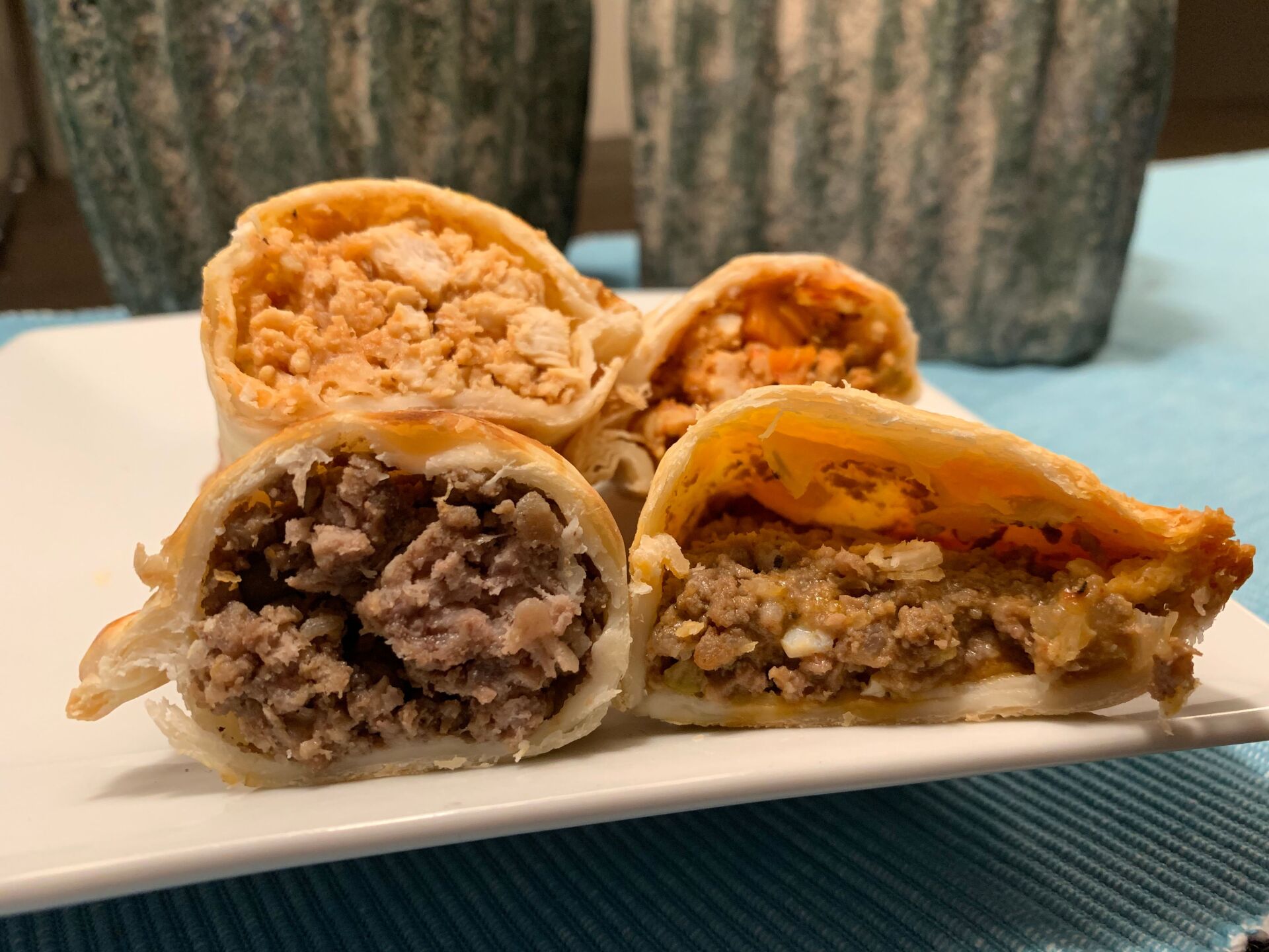 Close-up of four empanadas cut open, revealing various meat fillings, on a white plate.