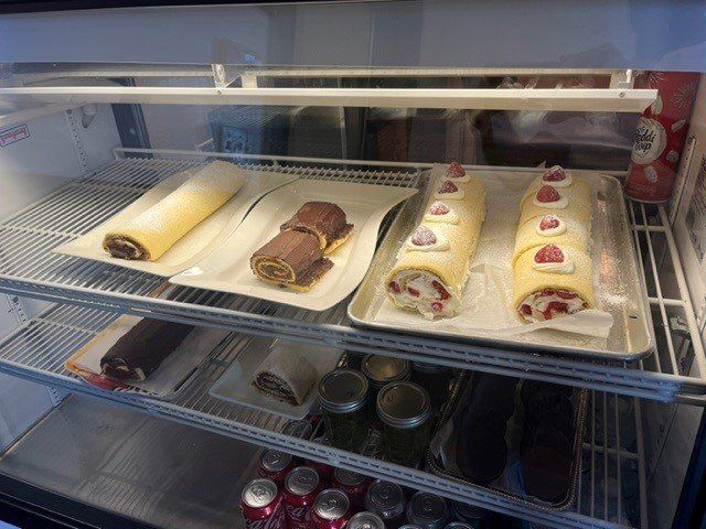 Cakes in a refrigerated display case, including swiss rolls with various fillings and toppings.