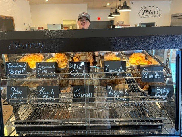 Person behind a glass display case filled with baked savory pastries, bakery.