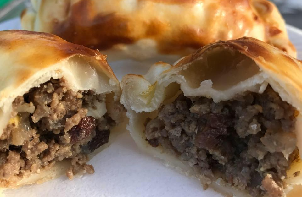 Close-up of a split empanada revealing a ground meat filling and flaky, golden crust.