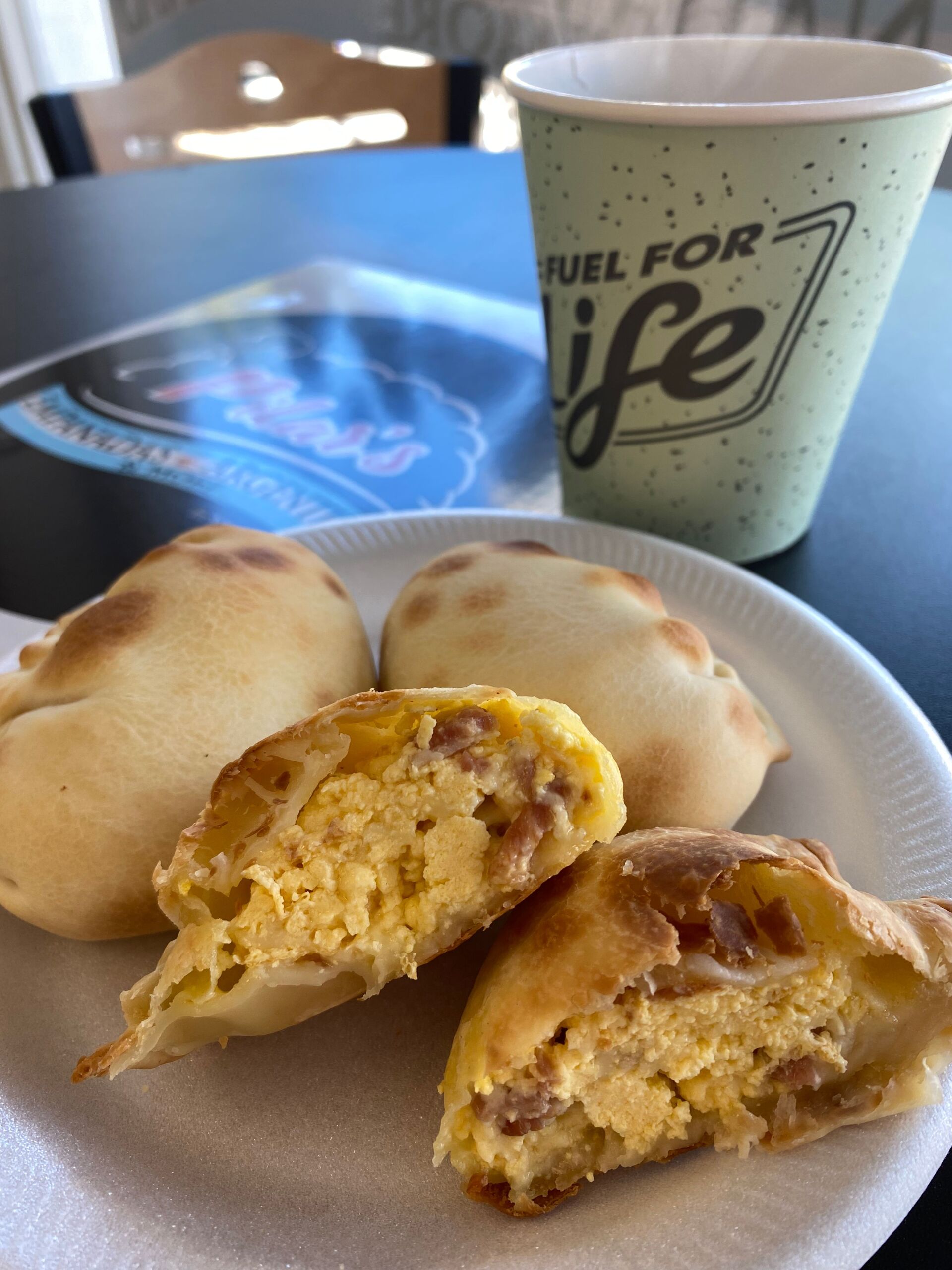 Plate with four empanadas, one cut open to show filling. Coffee cup in background.