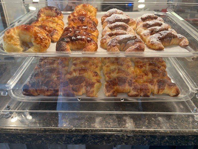 Croissants in a bakery display case, some dusted with powdered sugar, others glazed.