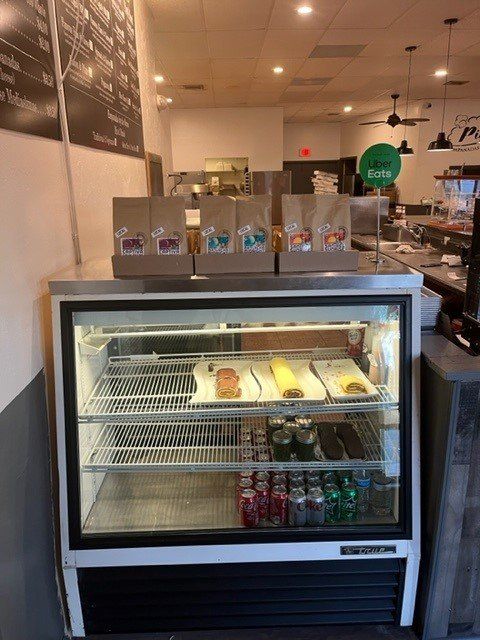 A refrigerated display case inside a cafe, holding pastries and drinks. Coffee bags are on top.