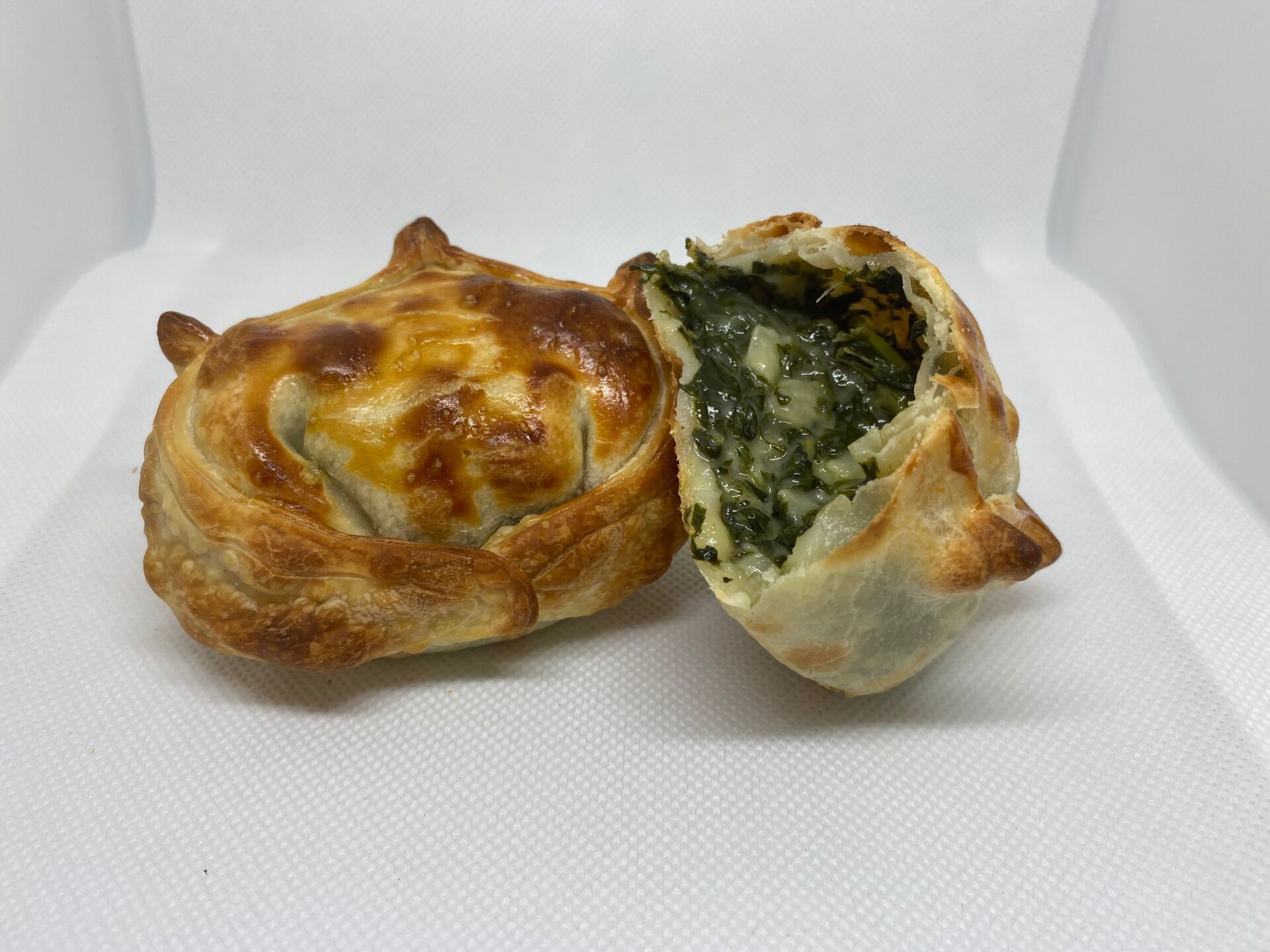 Two golden-brown, baked pastries. One is cut open, revealing a green spinach filling.