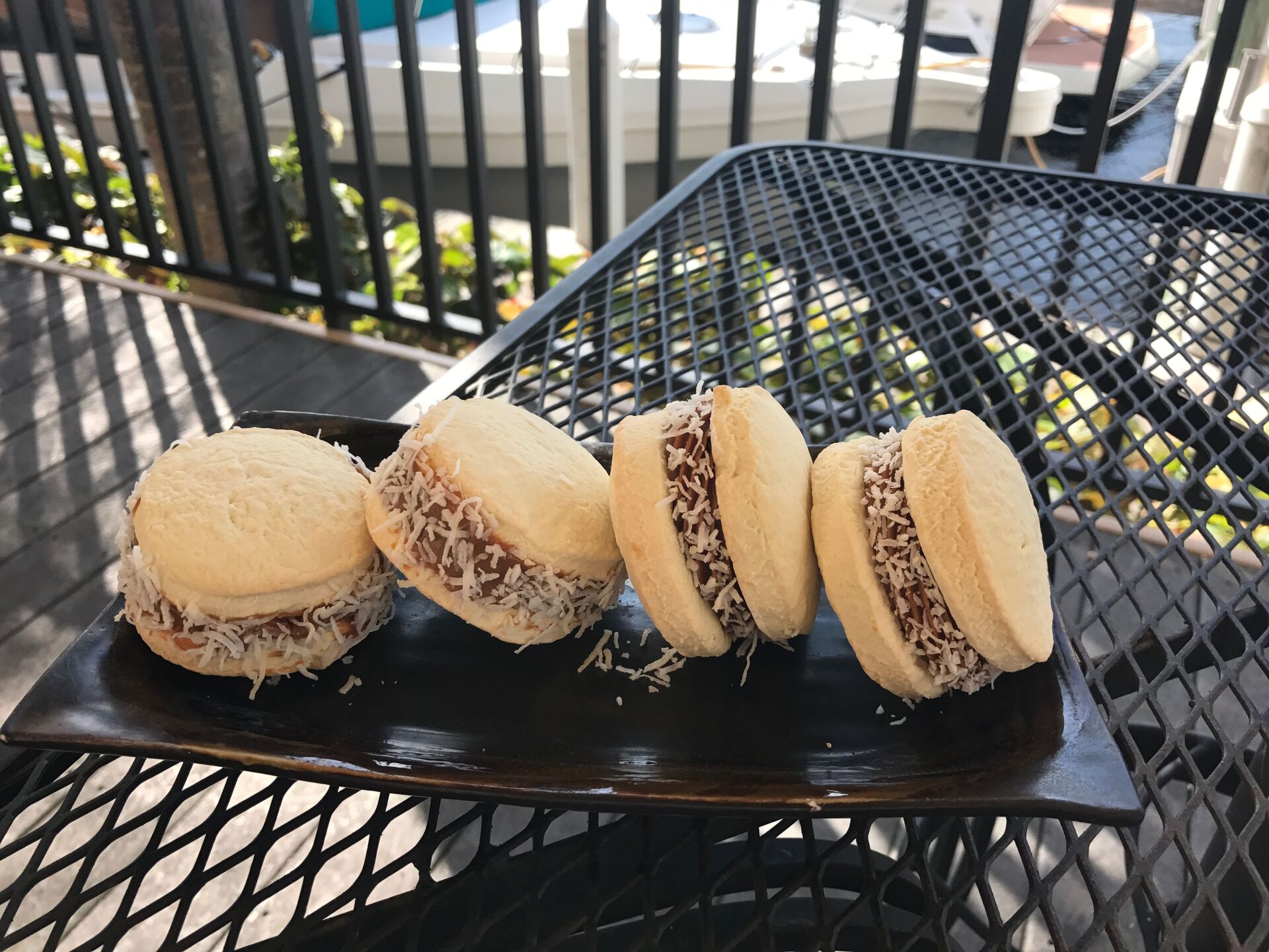Four alfajores with filling on a dark plate, outside on a sunny day.