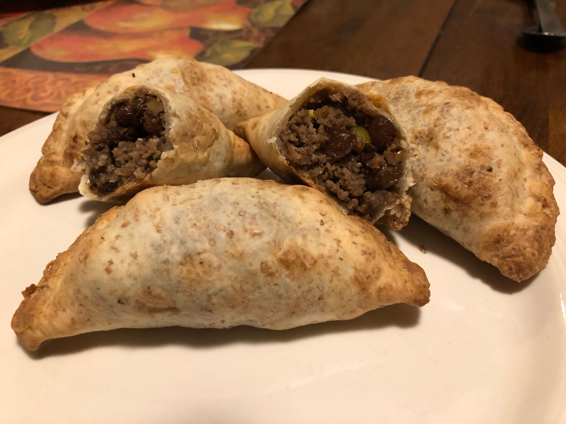 Plate of golden brown empanadas, one cut open revealing ground meat filling.
