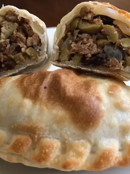 Empanadas, one cut open to show filling of meat, olives, and raisins; golden crust.